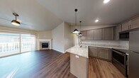 This single-floor home is designed with a modern, open-concept layout that seamlessly connects the kitchen, dining, and living areas. The living room is anchored by a stone-surround fireplace and benefits from vaulted ceilings that amplify the sense of space. Large sliding doors allow natural light to pour across the dark hardwood-style flooring, enhancing the warm, neutral color palette throughout.

The kitchen is well-appointed with taupe cabinetry, light granite countertops, a peninsula with an undermount sink, and stainless steel appliances including a refrigerator, range, and microwave. Stylish pendant lights hang above the peninsula, complementing the recessed lighting overhead.

The bedrooms are carpeted and bright, each featuring windows that bring in natural light. One bedroom includes a ceiling fan and wall-mounted climate control unit with a baseboard heater. Two bathrooms serve the home — one with a soaking tub and one with a walk-in shower — both featuring granite-topped vanities and wood-style flooring. A dedicated laundry area houses a full-size front-loading washer and dryer with overhead shelving, adding everyday convenience to this thoughtfully designed home.