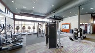 Located at 6963 E 109th Ave in Westminster, Colorado, this contemporary fitness center offers a well-appointed, single-floor layout designed to support a wide range of exercise routines. The space is anchored by an impressive wall of floor-to-ceiling windows that floods the gym with natural light, creating an open and energizing atmosphere. Exposed ductwork along the ceiling adds an industrial aesthetic that complements the modern design, while recessed lighting ensures the space is well-lit throughout.

The fitness floor is equipped with professional-grade cardio machines, including treadmills and ellipticals, all positioned to take advantage of the natural light and views. A prominent multi-function cable machine serves as a centerpiece for strength training, and additional free weights and equipment are thoughtfully arranged to maximize usability and flow. A large flat-screen television mounted on a feature wall adds an entertainment element to the space, enhancing the overall workout environment.

The flooring features a striped, multi-tone carpet in the exercise areas, providing both comfort and visual interest. Ceiling fans and a well-designed ventilation system ensure proper air circulation throughout. Overall, the space strikes a balance between functionality and modern design, making it a well-equipped destination for fitness in the Westminster community.