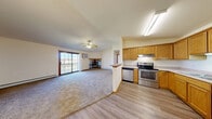 Located at 201 Air Park Dr in Watertown, Wisconsin, this well-appointed one-bedroom, one-bathroom unit offers a functional and comfortable single-floor layout. The open-concept living and dining area flows seamlessly into the kitchen, which features warm oak cabinetry, stainless steel appliances including a range, dishwasher, and refrigerator, and durable wood-look flooring. A breakfast bar peninsula provides additional counter space and casual dining options. The living room is carpeted and highlighted by a ceiling fan, a corner fireplace, and sliding glass doors that open onto a private balcony with outdoor views. The generously sized bedroom includes a ceiling fan, a window with natural light, and access to multiple closets, including a spacious walk-in closet with built-in wood shelving. The full bathroom features a wood-trimmed vanity with a lighted mirror, a soaking tub, and wood-look flooring. Additional conveniences include a dedicated laundry area and a hallway connecting the various spaces. Baseboard heating is present throughout, complemented by wall air conditioning units in the living and bedroom areas. Warm wood trim accents carry consistently throughout the unit, contributing to a cohesive and inviting aesthetic.