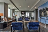 Located in Atlanta, GA, this sophisticated single-floor amenity space offers a well-appointed layout designed for both socializing and relaxation. The open floor plan flows seamlessly between distinct functional zones, unified by a consistent palette of neutral tones, patterned carpeting, and contemporary finishes.

The lounge area features an expansive seating arrangement with deep brown sofas, cobalt blue upholstered chairs with sleek metal frames, and a large leather ottoman, all positioned to take advantage of floor-to-ceiling windows that frame sweeping views of the Atlanta skyline. Natural light fills the space throughout the day, enhancing its modern, polished ambiance.

Adjacent to the lounge is a bar and dining area highlighted by amber pendant lights suspended above counter-height seating, with a granite-topped bar and mirrored backdrop adding depth and sophistication. High-top tables near the windows provide additional seating with panoramic city views.

A billiards room anchors one end of the space, featuring a full-size pool table set against teal-toned walls and glass partitions that overlook an outdoor terrace. Recessed lighting and tile flooring complete this recreational zone, creating a clean contrast to the carpeted lounge areas. Together, the zones offer a versatile, upscale environment ideal for gatherings and events.