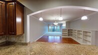 This single-floor residence offers a thoughtfully designed layout with a seamless flow between living spaces. The open-concept living and dining area is connected by an elegant arched passageway, with warm hardwood floors extending throughout. Pendant lighting and crown molding add refined detail, while a large sliding glass door draws in natural light and leads to an outdoor view. Built-in shelving along one wall provides functional display and storage space.

The kitchen is well-equipped, featuring rich dark wood cabinetry that extends to the ceiling, granite countertops, a decorative tile backsplash with an ornamental medallion accent, and a full suite of stainless steel appliances including a gas range, built-in microwave, dishwasher, and French door refrigerator. The tile flooring throughout the kitchen is durable and easy to maintain.

The bedrooms are carpeted and trimmed with crown molding, offering a quiet, comfortable atmosphere. The primary bathroom includes a soaking tub, a separate glass-enclosed shower, and tile flooring, while a secondary bathroom features a vanity with rich wood cabinetry and a separate tub enclosure. A dedicated laundry room with full-size washer and dryer and overhead cabinetry completes the layout.