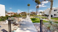 This property showcases a harmonious blend of Southwestern architecture and modern design, creating a tranquil desert retreat. The complex features crisp white stucco buildings with clean lines and red-tiled roofs, typical of the region. Lush landscaping contrasts beautifully with the arid surroundings, incorporating drought-resistant plants, succulents, and carefully placed palm trees.

The outdoor spaces are a highlight, offering various seating areas and communal gathering spots. A central courtyard boasts manicured lawns, paved walkways, and strategically placed shade structures. Modern pergolas provide comfortable seating areas, while raised planters with built-in benches offer additional relaxation spots.

The property's design emphasizes a connection to nature, with ample green spaces and rock gardens interspersed throughout. Thoughtful lighting, including modern bollard lamps, ensures the area is welcoming day and night. The overall ambiance is one of serenity and sophistication, perfect for those seeking a peaceful desert lifestyle with contemporary comforts.
