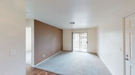 This single-story residence offers a practical and straightforward layout across several well-defined spaces. The living area is a comfortable, open room featuring plush carpeting, a distinctive brown accent wall, and a sliding glass door that provides direct access to an outdoor area while filling the room with natural light and views of the surroundings. Adjacent to the living area, the entryway transitions seamlessly to hard surface flooring, leading into the kitchen.

The kitchen is equipped with warm-toned wood cabinetry providing ample storage above and below the countertops. An L-shaped countertop layout offers generous workspace, complemented by a stainless steel sink beneath a window, a white electric range with an overhead vent, and a full-size refrigerator. The kitchen's hard surface flooring adds durability to this functional space.

The bedrooms are carpeted and bright, each featuring windows that invite natural light and outdoor views, creating a calm and airy atmosphere. The bathroom is finished with tile flooring and includes a glass-door shower enclosure, offering a clean and functional design. Throughout the unit, neutral tones and simple finishes create a cohesive, understated aesthetic.