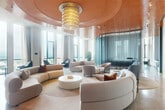 Located atop 7342 Wisconsin Avenue in Bethesda, MD, this penthouse lounge is an expansive, elegantly designed amenity space that blends bold architectural expression with refined comfort. The centerpiece of the lounge is a dramatic, multi-tiered copper ceiling adorned with a cascading sculptural chandelier, anchoring a generous seating area furnished with curved, modular sofas and curated lounge chairs arranged atop polished terrazzo floors. Floor-to-ceiling windows wrap the space, flooding the interior with natural light and offering sweeping views of the surrounding Bethesda skyline. The bar kitchen is a standout feature, showcasing rich teal marble countertops and backsplash, mirrored shelving, pendant lighting, and a sleek bar counter with seating — ideal for entertaining. A dedicated conference and dining area features a large communal table set beneath soaring ceilings and floor-to-ceiling windows, providing an inspiring setting for meetings or private gatherings. A casual dining nook with banquette seating, curated artwork, and soft accent lighting offers a more intimate retreat. The office area includes a thoughtfully designed built-in workspace with warm terracotta tones and brass accents. Throughout, a cohesive palette of copper, teal, and soft neutrals creates an atmosphere that is simultaneously vibrant and sophisticated.