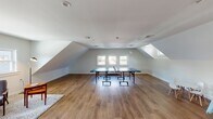Located at 703 Whitney Ave in New Haven, CT, this dedicated kids playroom is a thoughtfully designed recreational space that blends open-concept functionality with warm, inviting aesthetics. The room is characterized by its striking vaulted, sloped ceilings with skylights and multiple windows that flood the space with abundant natural light, creating an airy and cheerful atmosphere throughout.

The flooring features warm-toned hardwood planks that extend across the entire open area, providing a durable and attractive surface well-suited for active play. The generous floor plan offers ample room for a full-size ping-pong table at its center, while still accommodating a dedicated children's play corner equipped with a small table and chairs, a colorful play structure, and open space for imaginative play.

A cozy lounge nook is furnished with mid-century modern chairs and a footrest, positioned on a soft area rug — ideal for supervising adults or older children. A rich, dark wood credenza with a mid-century design adds a refined touch near the entrance, complemented by the bold, deep-toned solid wood entry door that serves as a striking architectural focal point. The clean white walls, recessed lighting, and multiple windows offering views of the surrounding neighborhood complete this bright and welcoming recreational retreat.