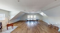 Located at 703 Whitney Ave in New Haven, CT, this dedicated kids playroom is a thoughtfully designed recreational space that blends open-concept functionality with warm, inviting aesthetics. The room is characterized by its striking vaulted, sloped ceilings with skylights and multiple windows that flood the space with abundant natural light, creating an airy and cheerful atmosphere throughout.

The flooring features warm-toned hardwood planks that extend across the entire open area, providing a durable and attractive surface well-suited for active play. The generous floor plan offers ample room for a full-size ping-pong table at its center, while still accommodating a dedicated children's play corner equipped with a small table and chairs, a colorful play structure, and open space for imaginative play.

A cozy lounge nook is furnished with mid-century modern chairs and a footrest, positioned on a soft area rug — ideal for supervising adults or older children. A rich, dark wood credenza with a mid-century design adds a refined touch near the entrance, complemented by the bold, deep-toned solid wood entry door that serves as a striking architectural focal point. The clean white walls, recessed lighting, and multiple windows offering views of the surrounding neighborhood complete this bright and welcoming recreational retreat.