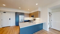 Located at 3405 SE Reed Dr. in Hillsboro, Oregon, this modern 2-bedroom, 2-bathroom residence offers a well-designed single-floor layout with contemporary finishes throughout. The open-concept kitchen and living area serves as the heart of the home, showcasing a striking blue peninsula with a crisp white quartz countertop, an undermount sink, and a full suite of stainless steel appliances including a French door refrigerator, electric range, built-in microwave, and dishwasher. Two-tone cabinetry combines warm wood-grain uppers with charcoal lower cabinets, complemented by a clean white tile backsplash and light hardwood-style flooring. The living area extends to a private balcony through a glass door, offering elevated views of the Hillsboro skyline. Both bedrooms feature plush carpeting and generous natural light, with the secondary bedroom capturing scenic neighborhood views through a large window. Each bedroom is served by a dedicated closet with multi-tier wire shelving systems, maximizing storage. The bathrooms reflect the same modern aesthetic, with matte black hardware accents, sleek gray cabinetry, and white countertops. Recessed lighting throughout adds a clean, polished ambiance to every room in this thoughtfully appointed residence.