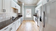 Located at 1193 Waxwing Dr, Building 1185 Unit B in Florence, SC, this two-floor residence combines classic architectural details with modern finishes throughout. The main living and dining areas are defined by striking embossed tin ceilings, elegant arched openings, and white decorative columns that add a refined, traditional character. Warm wood-look flooring flows through the open-plan living spaces, complemented by soft sage-green and neutral beige wall tones. Ceiling fans are present throughout, ensuring comfort in every room. The galley-style kitchen is well-equipped with stainless steel appliances, including a range, microwave, and refrigerator, paired with crisp white cabinetry, dark granite countertops, and a classic subway tile backsplash. A window above the sink allows natural light to fill the space. The primary bedroom features a tray ceiling with crown molding, adding an elevated sense of space, while additional bedrooms are finished with neutral tones and tile flooring. Bathrooms are thoughtfully appointed with granite-topped white vanities, undermount sinks, and soaking tubs with tile surrounds. The upper level is accessed via a staircase visible from the main living area, offering additional living space. Overall, the home presents a cohesive blend of decorative craftsmanship and practical design.