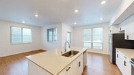 Located at 1932 NE 179th St in Ridgefield, WA, this single-story home offers four bedrooms and two full bathrooms within a thoughtfully designed floor plan. The interior features a consistent palette of crisp white walls, recessed lighting, and warm wood-tone flooring throughout the main living areas, creating a bright and welcoming atmosphere.

The kitchen serves as a central hub of the home, showcasing white shaker-style cabinetry with matte black hardware, light quartz countertops, stainless steel appliances including a refrigerator, microwave, and range, and an island with a single-basin sink. Multiple windows flood the space with natural light, and the open layout connects seamlessly to the adjacent living area.

The bedrooms are finished with neutral carpet and clean white walls, offering comfortable and versatile spaces. The primary bedroom includes a closet with built-in shelving. Both bathrooms are finished with wood-look flooring, white vanities with quartz countertops, large mirrors with vanity lighting, and brushed nickel fixtures. One bathroom features a full tub-shower combination.

A dedicated laundry area houses a stacked washer and dryer unit alongside additional shelving. Two hallways connect the rooms efficiently, completing this practical and modern single-floor home.