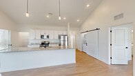 Located at 660 Aubrey Ln in Calabash, NC, this well-designed single-story home offers a thoughtful layout across two bedrooms and two bathrooms. The heart of the home is a bright, open-concept space combining the living room, dining area, and kitchen beneath soaring vaulted ceilings. The kitchen is outfitted with white shaker cabinetry, granite countertops, stainless steel appliances, a large center island, and pendant lighting. A stylish sliding barn door leads to a dedicated laundry area with stacked washer and dryer. Light wood-look flooring runs throughout the main living areas, complementing the clean, neutral palette. The hallway connects both bedrooms, each featuring ceiling fans, natural light from windows with views of the surrounding neighborhood, and generous closet space — four closets are distributed throughout the home. The bathrooms are finished with white vanities, matte black hardware, and glass-enclosed showers. The dining area opens to a patio through a glass door flanked by large windows, inviting abundant natural light. Additional highlights include a pantry, a utility room, and an attached garage with an automatic opener. The overall ambiance is clean, modern, and move-in ready.