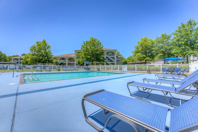 Pool deck with lounge chairs and umbrella seating overlooking apartment buildings, trees, and bright open sky - Parham Pointe