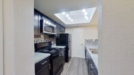 This single-floor, 2-bedroom, 2-bathroom residence offers a functional and thoughtfully designed layout. Wood-look flooring runs throughout, providing a cohesive and contemporary aesthetic across all living areas.

The kitchen is a standout feature, showcasing dark cabinetry paired with granite-style countertops, a mosaic tile backsplash, and black stainless appliances including a range, refrigerator, and microwave. A recessed skylight with track lighting brightens the space, creating an inviting atmosphere for cooking and entertaining.

The open living room is generously proportioned, featuring a wood-burning fireplace with a tile surround and large sliding glass doors fitted with vertical blinds that allow abundant natural light to fill the room.

Both bedrooms are comfortably sized, with the primary bedroom offering ample floor space. The rooms feature neutral-toned walls, wood-look flooring, and ceiling fixtures. Each bedroom includes access to closet space via clean white interior doors.

The two bathrooms are consistently styled, each equipped with dark vanity cabinetry, granite-style countertops, undermount sinks, and a full tub-shower combination set against white surround walls. Wood-look flooring carries through both bathrooms, maintaining the home's unified design language throughout.