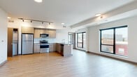 This contemporary single-floor residence offers a thoughtfully designed open-concept layout that seamlessly connects the kitchen and living areas. The kitchen is well-appointed with light wood cabinetry, stainless steel appliances including a refrigerator, electric range, and over-the-range microwave, complemented by a subway tile backsplash, quartz-style countertops, and a central island. Track lighting overhead and large black-framed windows flood the space with natural light while offering elevated urban views of the surrounding cityscape.

Light wood-tone flooring runs consistently throughout the entire unit, creating a cohesive and warm aesthetic. The bedrooms are generously sized, with clean white walls and large windows that capture outdoor views; at least one bedroom includes a walk-in closet. Two bathrooms serve the unit — one features a floating wood vanity, white countertop, a large mirror, and a walk-in shower with built-in shelving, while the second includes a full shower-tub combo and a matching floating vanity. Both bathrooms continue the light flooring theme. The overall ambiance is clean, modern, and move-in ready, reflecting a minimalist design sensibility with quality finishes.