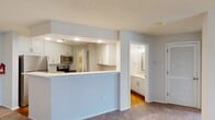 This single-story, one-bedroom, one-bathroom residence offers a thoughtfully arranged floor plan that maximizes its compact footprint. The open-concept living area flows seamlessly into a peninsula-style kitchen, which features white shaker cabinetry, light granite-style countertops, stainless steel appliances including a range and microwave, and recessed lighting overhead. The kitchen's raised breakfast bar provides a natural visual division between the cooking and living spaces, both of which feature neutral carpet and light gray walls.

The living room is bright and welcoming, anchored by a set of French doors fitted with white blinds that allow natural light to filter in. The bedroom is a comfortable, carpeted space with two closet doors and recessed lighting near the entry. The full bathroom is accessible from the bedroom area and includes warm hardwood-style flooring, a white vanity with granite-style countertops, and a full tub-shower combination. A dedicated laundry room houses a full-size washer and dryer beneath warm-toned oak cabinetry, adding practical convenience. Textured ceilings and a consistent neutral color scheme tie the entire space together cohesively.