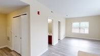 This single-floor residential unit offers a clean, functional layout with a neutral color palette and modern finishes throughout. The kitchen serves as a focal point, featuring rich wood-toned cabinetry, a peninsula island with a double-basin sink, light countertops, and black appliances including a refrigerator and range. Light wood-style plank flooring extends through the kitchen and main living areas, lending a cohesive, contemporary feel. A large window in the kitchen and dining area brings in generous natural light. The hallway area leads to multiple rooms, with a bathroom visible featuring matching dark wood vanity cabinetry. The bedrooms are carpeted in a warm neutral tone, providing comfort underfoot, and each room includes windows fitted with horizontal blinds that allow for adjustable natural light. Additional rooms with wood-style flooring offer flexible use as living or office space. The unit is equipped with ceiling-mounted smoke detectors and a fire alarm system, along with multiple closets for storage. The overall ambiance is bright, clean, and move-in ready, with a straightforward design that accommodates a variety of living arrangements.