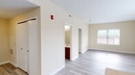 This single-floor residential unit offers a clean, functional layout with a neutral color palette and modern finishes throughout. The kitchen serves as a focal point, featuring rich wood-toned cabinetry, a peninsula island with a double-basin sink, light countertops, and black appliances including a refrigerator and range. Light wood-style plank flooring extends through the kitchen and main living areas, lending a cohesive, contemporary feel. A large window in the kitchen and dining area brings in generous natural light. The hallway area leads to multiple rooms, with a bathroom visible featuring matching dark wood vanity cabinetry. The bedrooms are carpeted in a warm neutral tone, providing comfort underfoot, and each room includes windows fitted with horizontal blinds that allow for adjustable natural light. Additional rooms with wood-style flooring offer flexible use as living or office space. The unit is equipped with ceiling-mounted smoke detectors and a fire alarm system, along with multiple closets for storage. The overall ambiance is bright, clean, and move-in ready, with a straightforward design that accommodates a variety of living arrangements.