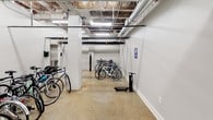 Jefferson Bike Shop is a single-level indoor bicycle storage and service facility designed to accommodate a large number of bikes in an organized, functional environment. The space features polished concrete floors throughout, providing a durable and easy-to-maintain surface well-suited to the demands of a high-use cycling facility. White-painted walls and structural columns lend a clean, utilitarian aesthetic, while the exposed ceiling reveals an industrial framework of large pipes, ductwork, and conduit running overhead, illuminated by fluorescent strip lighting that ensures consistent brightness throughout the room.

Multiple bike racks are positioned throughout the space, capable of accommodating a wide variety of bicycle styles, from road bikes to mountain bikes and children's bikes. A dedicated repair station with a mounted tool stand is centrally located, allowing users to perform basic maintenance conveniently. An air pump station is also available on-site, clearly marked with signage for easy identification. A secondary room, accessible through a door visible at one end of the space, provides additional utility. Signage throughout designates the area strictly for bicycle parking, reinforcing its purpose as a secure, well-equipped facility for cyclists.