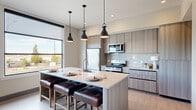 This thoughtfully designed single-floor unit offers a seamless open-concept layout that combines the kitchen and living room into one cohesive, light-filled space. The kitchen is a standout feature, showcasing flat-panel cabinetry in a warm wood-grain finish, a full suite of stainless steel appliances including a gas range, microwave, and refrigerator, and a large central island with a quartz countertop and seating for three. Three industrial-style pendant lights hang above the island, adding a modern focal point. Large windows flood the space with natural light and frame views of the surrounding cityscape and distant mountains, lending the interior an airy, connected feel. The living area provides a comfortable retreat with light wood-tone flooring, a wall-mounted television, and generous window placements that invite continued outdoor views. The entrance is accented by a large-scale landscape painting, setting an elegant tone upon arrival. The bathroom is finished with clean, contemporary details, including a dual-sink vanity with wood-grain cabinetry, a full-width mirror, mosaic tile flooring, and a glass-enclosed shower alongside a frosted-glass door enclosure. Throughout, the space maintains a neutral, modern palette that balances functionality with refined style.