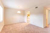 This two-story residence in Savannah, GA (31419) offers a straightforward, functional layout distributed across two floors. The main level features a carpeted living area illuminated by a pendant light fixture and a sliding glass door that opens to an outdoor view, allowing natural light to fill the space. A staircase visible from the living area provides access to the upper floor, and a window near the entry adds additional brightness to the lower level.

Adjacent to the living area, the dining space is also carpeted and connects directly to the kitchen through a doorway. The kitchen is equipped with warm wood-toned cabinetry, white countertops, a double stainless steel sink, a white range, and a dishwasher, providing practical functionality.

The upper floor hosts the bedrooms, each finished with plush carpeting and neutral wall tones. One bedroom features two side-by-side closets with built-in rods, while another includes a walk-in closet alongside an additional door. The full bathroom on this level is appointed with a double-sink vanity featuring wood cabinetry and stone-style countertops, a tiled tub-shower combination, and tile flooring throughout.