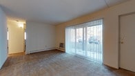 Located at 1901 W Chester Pike in Havertown, Pennsylvania, this single-floor space offers a straightforward and functional layout designed for comfortable everyday living. The main living area is generously sized, featuring wall-to-wall carpeting that adds warmth underfoot and a clean, neutral color palette throughout. A prominent set of floor-to-ceiling sliding glass doors fitted with vertical blinds allows an abundance of natural light to fill the room while providing direct views of the surrounding outdoor greenery. The large glazed opening also offers convenient access to the exterior. Climate control is provided by a combination of baseboard heating running along the perimeter of the room and a wall-mounted air conditioning unit, ensuring year-round comfort. The smooth, white ceiling and light-toned walls contribute to a bright, open atmosphere. The overall design is clean and understated, offering a blank canvas that is easy to personalize. Its single-level layout makes the space highly accessible, and its location along West Chester Pike places it within easy reach of local amenities, dining, and transportation options throughout the Havertown area.