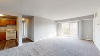 This single-floor unit offers a well-organized layout designed for comfortable everyday living. The living area is generously sized, finished with neutral-toned carpet and light gray walls that create a bright, clean atmosphere. A sliding glass door leads to a private balcony, allowing natural light to fill the space while providing views of surrounding greenery. An HVAC vent is integrated into the ceiling, ensuring year-round climate control.

Adjacent to the living area, the kitchen features warm-toned oak cabinetry extending to the upper walls for ample storage, complemented by light granite-style countertops, a double sink, and wood-look vinyl flooring. White appliances, including a gas range and refrigerator, are included.

The bedrooms are carpeted and finished with the same neutral palette, each offering generous proportions. One bedroom includes a walk-in closet with built-in shelving, providing substantial storage. A window in one bedroom frames views of mature trees, enhancing the connection to the outdoors.

The bathroom includes a full tub-shower combination with white tile surround, a wood-toned vanity with a white countertop, and wood-look flooring, completing the unit's functional and cohesive design.