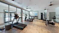 Located at 1743 Central Park Rd in Charleston, SC, this single-floor fitness center is thoughtfully designed to support a well-rounded exercise routine. The space features cork flooring throughout, providing a resilient and comfortable surface underfoot, while recessed lighting and ceiling fans maintain a bright and well-ventilated environment.

The cardio area is equipped with multiple treadmills and elliptical machines, positioned alongside floor-to-ceiling glass walls that invite abundant natural light and provide views of the outdoor surroundings. A dedicated strength training zone includes a multi-functional cable machine, a weight bench, a full dumbbell rack ranging across a variety of weights, stability balls, and a stationary spin bike — offering a comprehensive setup for both beginner and advanced fitness levels.

Mounted flat-screen televisions are positioned throughout the space to keep users entertained during workouts. Glass partition walls divide the fitness floor from an adjacent recreation room, which is visible through the transparent panels and appears to include a game table, adding a social element to the facility.

The overall design is clean and modern, with white walls, open sight lines, and a layout that maximizes usable floor space. The generous glazing on multiple sides of the room ensures the space feels open and connected to the outdoors, creating an energizing atmosphere for exercise.