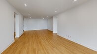 This well-designed 2-bedroom, 2-bathroom residence offers a thoughtfully laid-out single-floor plan finished with consistent light wood flooring and crisp white walls throughout. The open kitchen is a standout feature, outfitted with light wood cabinetry extending to the ceiling, marble-veined quartz countertops and backsplash, matte black hardware, and a full suite of stainless steel appliances including a range, dishwasher, and refrigerator. Recessed lighting illuminates the space efficiently. The living area is generously proportioned with large windows framing city skyline views, filling the room with natural light. The spacious primary bedroom also benefits from oversized windows with urban views and includes access to a walk-in closet with built-in shelving and hanging rods. Both bathrooms are finished to a high standard, featuring marble-veined quartz vanity countertops, light wood cabinetry with open shelving, matte black fixtures and hardware, tile flooring, and framed rectangular mirrors. The second bedroom is well-sized and bright, served by recessed lighting. Clean architectural lines, a neutral palette, and consistent modern finishes create a cohesive, contemporary ambiance throughout the entire residence.