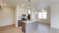 This well-appointed single-floor residence offers a thoughtfully designed open-concept layout that seamlessly connects the kitchen, dining, and living areas. The kitchen is a standout feature, showcasing a large central island with a white quartz countertop and an integrated sink, complemented by two sleek pendant lights overhead. Two-toned cabinetry pairs crisp white upper cabinets with warm wood-grain lower cabinets, while a full suite of stainless steel appliances — including a refrigerator, electric range, and microwave — provides a polished, contemporary finish. Light hardwood-style flooring flows throughout the main living area, enhancing the bright and airy atmosphere created by large windows and a sliding glass door that opens to a private balcony with views of surrounding greenery. The living space is generously proportioned and filled with natural light. Both bedrooms feature plush neutral carpet and windows that invite natural light, with one bedroom also equipped with a ceiling fan. Two full bathrooms mirror each other in design, each offering a soaking tub with shower, a wood-grain vanity with white countertop, a large mirror, and neutral tile flooring. A dedicated in-unit laundry area with a full-size washer and dryer rounds out this functional and modern residence.
