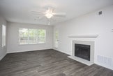 This single-story residence offers a well-organized layout with a variety of functional spaces throughout. The open living area is a standout, featuring durable wood-style plank flooring, a ceiling fan, and a tiled fireplace framed by a classic white mantel. Large windows fitted with blinds allow natural light to fill the room, creating a bright and welcoming atmosphere. The living space flows directly into the dining area and kitchen, which is equipped with white shaker-style cabinetry, granite-look countertops, stainless steel appliances including a gas range, microwave, and refrigerator, and a peninsula that provides additional prep and seating space. Adjacent to the kitchen, a dedicated laundry closet offers in-unit hookups for added convenience. The bedrooms are carpeted and offer a soft, comfortable feel, with multiple windows providing natural light and views of surrounding greenery. One bedroom includes direct access to a walk-in closet and an en-suite bathroom. Both bathrooms feature wood-style flooring, tub-shower combinations, and clean white fixtures with granite-topped vanities. Textured ceilings are consistent throughout the unit, contributing to its cohesive, residential character.