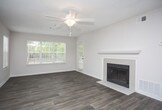 This single-story residence offers a well-organized layout with a variety of functional spaces throughout. The open living area is a standout, featuring durable wood-style plank flooring, a ceiling fan, and a tiled fireplace framed by a classic white mantel. Large windows fitted with blinds allow natural light to fill the room, creating a bright and welcoming atmosphere. The living space flows directly into the dining area and kitchen, which is equipped with white shaker-style cabinetry, granite-look countertops, stainless steel appliances including a gas range, microwave, and refrigerator, and a peninsula that provides additional prep and seating space. Adjacent to the kitchen, a dedicated laundry closet offers in-unit hookups for added convenience. The bedrooms are carpeted and offer a soft, comfortable feel, with multiple windows providing natural light and views of surrounding greenery. One bedroom includes direct access to a walk-in closet and an en-suite bathroom. Both bathrooms feature wood-style flooring, tub-shower combinations, and clean white fixtures with granite-topped vanities. Textured ceilings are consistent throughout the unit, contributing to its cohesive, residential character.