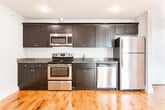 Located at 134 Sussex Ave in Newark, NJ, this single-floor unit offers a clean, modern living environment with consistent finishes throughout. The living areas are characterized by warm hardwood flooring and neutral gray walls that reflect abundant natural light, as evidenced by the crisp window shadows cast across the rooms. The open, well-proportioned spaces provide a comfortable and functional layout.

The kitchen is a standout feature, outfitted with rich dark espresso cabinetry, granite countertops, and a full suite of stainless steel appliances including a refrigerator, electric range, over-the-range microwave, and dishwasher. Recessed lighting and continued hardwood flooring tie the kitchen seamlessly into the rest of the unit. An electrical panel is conveniently accessible within the kitchen area.

The bathroom is finished with large-format marble-look porcelain tile flooring and wall accents, a full soaking tub with shower, a wall-mounted toilet, and a dark wood vanity, presenting a crisp and polished aesthetic. Throughout the unit, white trim and panel doors add a clean architectural detail. This space combines updated finishes with a straightforward, functional design well-suited for Newark's urban setting.