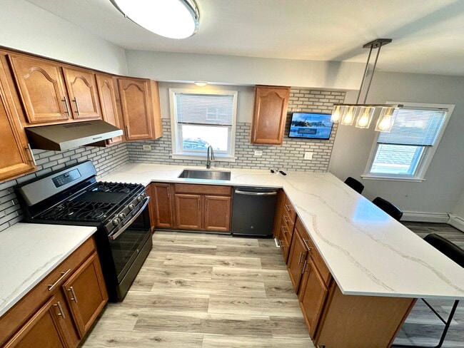 Peninsula kitchen with quartz counters and three counter chairs. - 671 56th St
