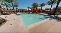 This Mediterranean-inspired resort complex boasts an array of high-end amenities set within a meticulously landscaped environment. The centerpiece is a sprawling, crystal-clear pool surrounded by towering palm trees and comfortable lounge chairs with vibrant orange umbrellas. The architecture showcases a harmonious blend of cream-colored stucco buildings with terracotta tile roofs, creating a cohesive and inviting atmosphere.

Throughout the grounds, thoughtfully designed outdoor spaces invite relaxation and socialization. Pergolas with sturdy columns provide shaded seating areas, while manicured gardens featuring a variety of plants and shrubs add natural beauty. The complex also includes a spa pool with invigorating jets, perfect for unwinding.

Ample paved walkways connect various areas of the resort, lined with lush greenery and accent lighting. Modern outdoor furniture, including plush sectionals and sleek lounge chairs, dot the landscape, offering numerous spots for guests to enjoy the serene surroundings. The overall design seamlessly blends indoor and outdoor living, with large arched windows and doors connecting interior spaces to the exterior amenities.

This resort complex epitomizes luxury living in a warm climate, providing residents with a resort-like experience in their everyday surroundings. The attention to detail in both the landscaping and architectural elements creates an ambiance of refined elegance and tranquility.