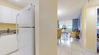 This single-floor residence offers a thoughtfully designed layout that balances comfort and style. The living room serves as a central highlight, featuring soft blue walls adorned with decorative panel molding, large floor-to-ceiling sliding glass doors that flood the space with natural light, and direct access to a private balcony with outdoor views. White tile flooring runs throughout the main living areas, reflecting light and enhancing the open, airy feel.

The dining area is positioned adjacent to the living room and kitchen, anchored by a round glass-top table beneath a modern overhead fixture. A pass-through granite countertop connects the dining space to the kitchen, which is outfitted with white cabinetry, granite countertops, white appliances including a refrigerator, dishwasher, oven, and microwave, and tile flooring that carries through from the main living areas.

The bedroom is a calm and generously sized retreat, finished with soft blue-gray walls, plush carpeting, and a window that allows natural light to filter in. A full bathroom is conveniently accessible and features a tub-shower combination with tile flooring and warm neutral tones. Throughout the residence, the design palette of blues, creams, and whites creates a cohesive and serene atmosphere.