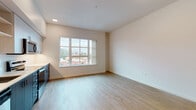 Located at 180 E 5th Ave in Eugene, Oregon, this single-floor unit offers a clean, modern design with a thoughtfully organized layout. Light wood flooring flows throughout, complementing the bright, neutral walls and creating a warm, welcoming atmosphere.

The open living area is anchored by a large multi-pane window that frames views of the surrounding Eugene cityscape and treetops, filling the space with natural light. The area provides ample room for flexible furniture arrangements.

The kitchen is well-appointed with a full suite of stainless steel appliances, including a refrigerator, electric range, over-the-range microwave, and dishwasher. Two-tone cabinetry pairs dark lower cabinets with lighter upper cabinets, accented by a clean white countertop and tile backsplash. Open shelving adds a contemporary touch.

A dedicated hallway leads to the additional rooms, including a bathroom featuring wood-look tile flooring, a dark-toned floating vanity with a white countertop and undermount sink, a full mirror, and chrome fixtures. The space is neatly designed for both function and style.

Recessed lighting throughout ensures consistent illumination, while the unit's layout maximizes usability. An electrical panel is conveniently accessible within the unit. Overall, the space presents a modern, move-in-ready environment in a well-situated Eugene location.