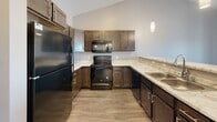 This single-floor residence at 2200 S Ellis Rd in Sioux Falls, South Dakota offers a well-appointed layout with thoughtfully selected finishes throughout. The kitchen serves as a central highlight, featuring rich dark-stained cabinetry paired with light granite-style countertops, black appliances including a refrigerator, electric range, and built-in microwave, and a double sink. Vaulted ceilings rise above the kitchen and living area, enhancing the sense of openness, while pendant lighting adds a polished touch. A raised breakfast bar separates the kitchen from the living space, creating a natural flow between the two areas. Wood-look luxury vinyl plank flooring extends through the main living and kitchen areas, providing durability and visual continuity. The bedroom is carpeted and bathed in natural light through a window offering neighborhood views. The full bathroom includes a dark-stained vanity with ample cabinet and drawer storage, a light countertop, a well-lit mirror, and a soaking tub with shower. A dedicated laundry area accommodates a full-size side-by-side washer and dryer with overhead shelving for added storage convenience.