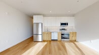 Located at 347 N Queen St in the heart of Lancaster, PA, this thoughtfully designed one-bedroom, one-bathroom unit offers a clean, modern aesthetic throughout. Light hardwood flooring runs continuously across the open-concept living and kitchen area, creating a bright and cohesive feel. The kitchen is outfitted with full-height white cabinetry, warm wood-toned lower cabinets, a tiled backsplash, and a complete suite of stainless steel appliances including a French door refrigerator, electric range, built-in microwave, and dishwasher — providing both style and functionality. A bright hallway with recessed lighting connects the living area to the private quarters. The bedroom is a well-proportioned retreat featuring light hardwood floors, a double-door closet, and a large window that fills the room with natural light and offers views of the surrounding Lancaster cityscape. A secondary window with a city view is also visible from the living area. The bathroom is finished with large-format gray tile flooring and a glass-enclosed walk-in shower with earthy tile surround, lending a clean, spa-like quality. Throughout the unit, crisp white walls, recessed lighting, and minimalist finishes contribute to a modern, move-in-ready ambiance.