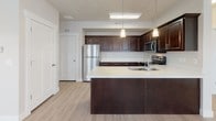 This single-floor residence is designed with a cohesive, modern aesthetic that emphasizes clean lines and functional living. The kitchen serves as a standout feature, outfitted with rich dark-stained cabinetry, white quartz countertops, and a full suite of stainless steel appliances, including a range, microwave, refrigerator, and dishwasher. A double-basin undermount sink and pendant lighting add refined detail, while the layout flows seamlessly into the open living and dining areas.

The living spaces are finished with light wood-tone flooring that enhances the bright, airy atmosphere created by multiple windows fitted with white blinds. A ceiling fan provides additional comfort, and a door provides direct access to the exterior. Track lighting and pendant fixtures supplement natural light throughout the common areas.

The bedroom is carpeted and features corner windows that allow natural light from multiple angles, along with a ceiling fan overhead. An adjacent walk-in closet offers built-in shelving and dual hanging rods, providing generous storage capacity.

The bathroom is finished with the same dark cabinetry and white countertop found in the kitchen, paired with an undermount sink, a large mirror, and globe-style vanity lighting, maintaining a consistent design language throughout the unit.