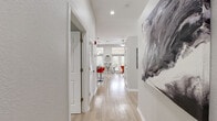 This single-floor unit offers a thoughtfully designed open-concept layout that maximizes every square foot. A light-filled hallway with recessed lighting and light wood-tone flooring provides an inviting entry, with large-scale abstract wall art setting a modern tone from the start.

The combined kitchen and living area serves as the heart of the space. The kitchen is well-equipped with rich warm-toned wood cabinetry, granite countertops, stainless steel appliances including a full-size refrigerator, electric range, microwave, and dishwasher. A central island with pendant lighting above and bar seating offers additional prep and dining space, complemented by a dedicated built-in desk area.

The living area features vaulted ceilings and a ceiling fan, with French doors that open to an outdoor area and flood the room with natural light and views of surrounding greenery. The layout comfortably accommodates a seating arrangement with a glass coffee table and open shelving unit.

The bathroom is clean and modern, featuring a walk-in glass shower with tile surround, a wooden vanity with a white countertop, a large mirror, and light wood flooring that ties back to the rest of the unit. Throughout the space, the neutral gray and white palette, recessed lighting, and cohesive flooring create a bright, contemporary ambiance.