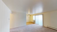 This single-floor unit offers a practical and straightforward layout with consistent finishes throughout. The living area is spacious, featuring neutral-toned carpet and light yellow walls that create a bright, airy feel. A large sliding glass door fitted with vertical blinds allows natural light to fill the space while providing outdoor access. Baseboard heaters along the walls ensure efficient climate control throughout the unit.

The kitchen is well-appointed with warm-toned wood cabinetry offering ample storage, light granite-style countertops, a double stainless steel sink, and light hardwood flooring. A skylight panel overhead adds brightness to the cooking area, which also includes a white appliance suite.

The bedrooms are comfortably sized, each featuring plush carpet, ceiling fans with integrated lighting, and sliding-door closets with built-in hanging rods. Windows dressed with vertical blinds allow natural light while maintaining privacy. Baseboard heaters are present in each room for individual comfort.

The bathroom is clean and functional, featuring a tiled tub and shower surround with chrome fixtures, a toilet, and a towel bar. The unit's overall design emphasizes practicality and comfort with a neutral, move-in-ready aesthetic.