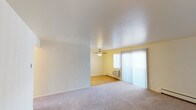 This single-floor unit offers a practical and straightforward layout with consistent finishes throughout. The living area is spacious, featuring neutral-toned carpet and light yellow walls that create a bright, airy feel. A large sliding glass door fitted with vertical blinds allows natural light to fill the space while providing outdoor access. Baseboard heaters along the walls ensure efficient climate control throughout the unit.

The kitchen is well-appointed with warm-toned wood cabinetry offering ample storage, light granite-style countertops, a double stainless steel sink, and light hardwood flooring. A skylight panel overhead adds brightness to the cooking area, which also includes a white appliance suite.

The bedrooms are comfortably sized, each featuring plush carpet, ceiling fans with integrated lighting, and sliding-door closets with built-in hanging rods. Windows dressed with vertical blinds allow natural light while maintaining privacy. Baseboard heaters are present in each room for individual comfort.

The bathroom is clean and functional, featuring a tiled tub and shower surround with chrome fixtures, a toilet, and a towel bar. The unit's overall design emphasizes practicality and comfort with a neutral, move-in-ready aesthetic.