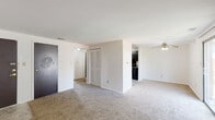 Located at 1301 N Whitcomb Ave in Indianapolis, Indiana, this single-floor unit offers two bedrooms and one bathroom across a comfortable and functional layout. The open living area is a standout feature, bathed in natural light streaming through a large sliding glass door that leads to an outdoor balcony. A ceiling fan anchors the living space, which is finished with wall-to-wall carpeting that extends throughout the unit. The layout flows from the living area toward a hallway that connects the bedrooms, bathroom, and closet spaces. The primary bedroom is generously sized, offering ample room for furniture arrangement, and features its own closet. The second bedroom is bright and well-proportioned, with a window that brings in natural light. Both bedrooms are carpeted and feature white walls, providing a clean, neutral backdrop. The bathroom includes a full tub and shower combination with white tile surround, a toilet, and a dark-cabinetry vanity with a granite-style countertop and tile flooring. The kitchen features dark cabinetry, visible from the main living area. Two closets provide practical storage throughout the unit. The overall ambiance is clean, simple, and functional, suited for everyday living.