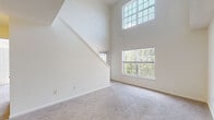 Located at 1 Avalon Way in Shrewsbury, Massachusetts, this two-floor residence offers a thoughtfully designed layout with bright, airy interiors throughout. The main living area immediately impresses with soaring double-height ceilings and a wall of large windows, including an elevated transom window, that flood the space with natural light and frame views of the surrounding greenery. Plush wall-to-wall carpeting adds warmth and comfort underfoot.

The kitchen is efficiently designed in a galley style, featuring white cabinetry, dark countertops, tile flooring, and a full suite of black appliances including a gas range, refrigerator, dishwasher, and built-in microwave. A peninsula with counter seating provides a natural transition into the living area. Conveniently positioned off the kitchen is an in-unit stacked washer and dryer.

The upper level offers an open loft-style landing with a ceiling fan, carpeted floors, and a partial railing that overlooks the main living space below. Multiple bedrooms are generously sized with carpet, neutral walls, and large windows offering pleasant outdoor views. The bathrooms are clean and functional, one featuring a tiled tub-shower combo, white vanity cabinetry, and a large mirror, while a second bath provides a streamlined vanity with tile flooring.