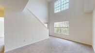 Located at 1 Avalon Way in Shrewsbury, Massachusetts, this two-floor residence offers a thoughtfully designed layout with bright, airy interiors throughout. The main living area immediately impresses with soaring double-height ceilings and a wall of large windows, including an elevated transom window, that flood the space with natural light and frame views of the surrounding greenery. Plush wall-to-wall carpeting adds warmth and comfort underfoot.

The kitchen is efficiently designed in a galley style, featuring white cabinetry, dark countertops, tile flooring, and a full suite of black appliances including a gas range, refrigerator, dishwasher, and built-in microwave. A peninsula with counter seating provides a natural transition into the living area. Conveniently positioned off the kitchen is an in-unit stacked washer and dryer.

The upper level offers an open loft-style landing with a ceiling fan, carpeted floors, and a partial railing that overlooks the main living space below. Multiple bedrooms are generously sized with carpet, neutral walls, and large windows offering pleasant outdoor views. The bathrooms are clean and functional, one featuring a tiled tub-shower combo, white vanity cabinetry, and a large mirror, while a second bath provides a streamlined vanity with tile flooring.