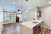 This single-floor residence offers a thoughtfully designed layout that balances functional living spaces with modern finishes throughout. The open-concept kitchen serves as a central feature, equipped with dark espresso-toned cabinetry, light quartz countertops, a double stainless steel sink with a matte black faucet, and stainless steel appliances including a full-size refrigerator. A peninsula with pendant lighting connects the kitchen seamlessly to the living area, which is outfitted with a ceiling fan and recessed lighting. Wood-look plank flooring flows consistently throughout the main living spaces, contributing to a cohesive and warm aesthetic. Neutral-toned walls provide a clean backdrop across all rooms. Bedrooms are well-sized, each featuring windows fitted with horizontal blinds that allow for natural light control. The bathroom includes a vanity with quartz countertop, a round mirror with black trim, and a walk-in shower. A dedicated laundry area houses a full-size front-loading washer and dryer with overhead shelving. An attached garage with a concrete floor and electrical panel completes the unit, offering practical storage and parking.