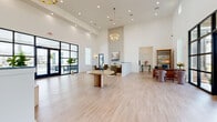 Located in Fairhope, Alabama, this single-story community clubhouse offers a generously sized, open-plan interior designed with a clean, contemporary coastal aesthetic. The grand main hall immediately impresses with soaring ceilings, light-toned hardwood flooring, and an abundance of natural light streaming through dramatic floor-to-ceiling black-framed glass doors that open directly to an outdoor pool and lounge area. A striking shiplap accent wall anchors the space, complemented by an elegant gold chandelier that adds a refined, upscale touch.

The living area is thoughtfully arranged with comfortable seating, a shiplap-backed media wall, and a cozy lounge nook, creating an inviting atmosphere for relaxation and socializing. A reception-style counter provides a defined transition between the main hall and surrounding areas. The dining space features intimate seating beside tall windows, offering pleasant outdoor views and ample natural light.

The kitchen is well-appointed with sage-gray shaker cabinetry, gold hardware, crisp white quartz countertops, and a full suite of stainless steel appliances including a wall oven, dishwasher, and refrigerator. A decorative mirror adds visual depth to the kitchen's clean lines. Throughout the space, the bright white walls, light wood floors, and curated furnishings create a cohesive, welcoming environment ideal for community gatherings.