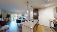 This single-floor residence is thoughtfully designed with a contemporary aesthetic and an open, flowing layout. The kitchen serves as a central hub of the home, featuring granite countertops, a peninsula island with pendant lighting overhead, stainless steel appliances, and a mix of dark and light wood cabinetry. Wood-look flooring runs through the kitchen and extends into the main living area, enhancing visual continuity.

The living room is generously proportioned, bathed in natural light from large sliding glass doors that open onto a private balcony, offering outdoor views of surrounding greenery. Built-in shelving provides additional display and storage options within the living space.

The bedroom offers a calm retreat, carpeted for comfort, with a large window that invites natural light and outdoor views. A ceiling fan adds functional comfort, and a spacious walk-in closet with a sliding barn-style door provides ample storage. A second bedroom features its own window with a built-in bench seat.

The bathroom is clean and practical, finished with wood-look flooring, a tub-shower combination, and a dark wood vanity with a white countertop. Neutral tones and modern fixtures are consistent throughout, giving the entire residence a cohesive, well-curated feel.