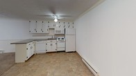 This single-floor, one-bedroom, one-bathroom unit offers a practical and straightforward layout. The living room is finished with wall-to-wall carpeting, crown molding, and a ceiling fan with light fixture. A sliding glass door opens to a balcony, allowing natural light to filter into the space and providing outdoor views of the surrounding building exterior. A baseboard heating unit runs along the wall, and a wall-mounted air conditioning unit ensures year-round comfort.

The kitchen features tile flooring, white upper and lower cabinetry with black hardware, granite-style countertops, and a full suite of white appliances including a refrigerator, electric range, microwave, and dishwasher. Crown molding and a ceiling fan with lighting complete the kitchen space.

The bedroom is carpeted and includes a ceiling fan, a window with natural light, baseboard heating, and crown molding, creating a calm and functional environment.

The bathroom is finished in white tile and includes a tub-shower combination, a toilet, a single vanity sink with under-cabinet storage, and a mirrored medicine cabinet. The overall aesthetic throughout the unit is clean, neutral, and move-in ready.