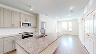 Located at 620 W Due West Ave in Nashville, TN, this well-appointed 2-bedroom, 2-bathroom residence offers a thoughtfully designed single-level layout. The open-concept living and kitchen area serves as the heart of the home, where light hardwood flooring flows seamlessly throughout. The kitchen is a standout feature, equipped with stainless steel appliances including a French door refrigerator, electric range, built-in microwave, and dishwasher. A generous granite-topped island with an undermount sink provides both prep space and casual seating, while soft gray shaker-style cabinetry and a white tile backsplash complete the modern aesthetic. The living room benefits from natural light through large windows and connects directly to an exterior door. The primary bedroom is a comfortable retreat with a ceiling fan and ample space. Each bathroom features granite vanity countertops, gray cabinetry, and hardwood-style flooring, maintaining the consistent design language found throughout the unit. Additional built-in shelving offers convenient storage solutions. The clean, neutral color palette and modern finishes create a bright, cohesive ambiance throughout this Nashville residence.