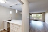 Located on 110 Street NW in Edmonton's vibrant Oliver neighbourhood, this one-bedroom unit offers a thoughtfully designed layout across a single floor. The open-concept living and kitchen area creates a cohesive, airy feel throughout the main space. Light-toned laminate hardwood flooring runs consistently underfoot, complemented by neutral warm-grey walls and a textured ceiling finish that adds subtle character.

The renovated kitchen is a standout feature, showcasing crisp white cabinetry with brushed nickel hardware, light quartz countertops, a undermount stainless steel sink, and stainless steel appliances including a full-height refrigerator and dishwasher. Elegant pendant lighting illuminates the kitchen peninsula, which is partially open to the living area via a structural column, maintaining defined zones while preserving the open feel.

The spacious living room receives generous natural light through large sliding windows and a glass-panel balcony door. The balcony itself offers pleasant views of mature trees lining the street below. The generously sized primary bedroom provides a comfortable private retreat.

Baseboard heating is present throughout, and the overall aesthetic is clean, modern, and move-in ready, making this a well-appointed unit in a convenient urban location.
